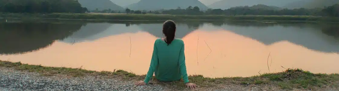 junge Frau sitzt an ruhigem Seeufer
